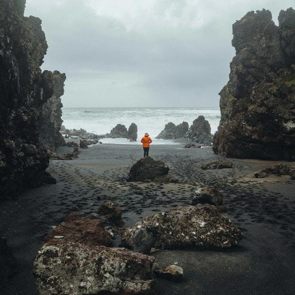 Traveller in Orange Windbreaker Standing on a Volcanic Black Beach on Snaefellsnes Peninsula Day Tour